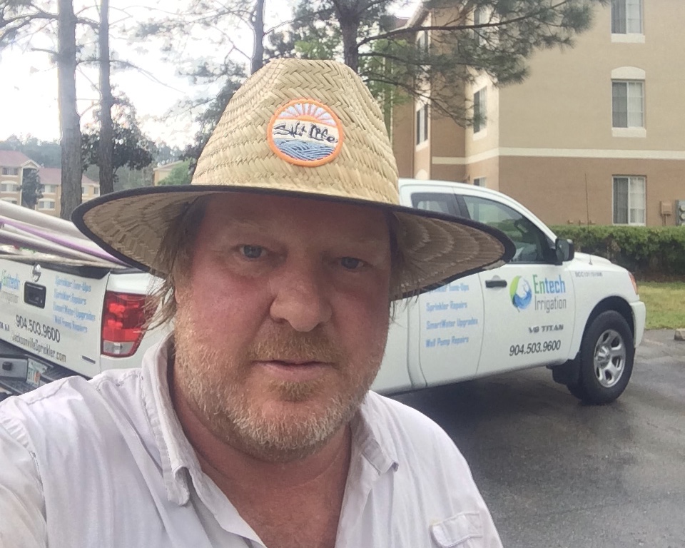 Andrew Brockman wearing his straw work hat in front of two Entech Irrigation trucks in Jacksonville